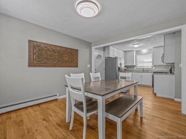 dining space featuring a baseboard heating unit, a textured ceiling, and light hardwood / wood-style floors