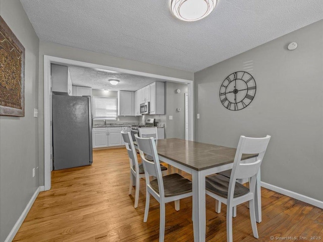 dining area with sink, a textured ceiling, and light wood-type flooring