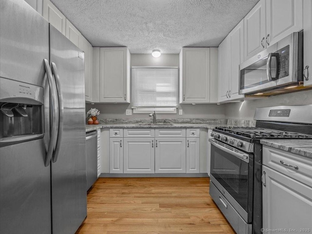 kitchen featuring sink, appliances with stainless steel finishes, a textured ceiling, white cabinets, and light wood-type flooring