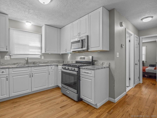 kitchen featuring sink, white cabinets, light hardwood / wood-style floors, stainless steel appliances, and light stone countertops