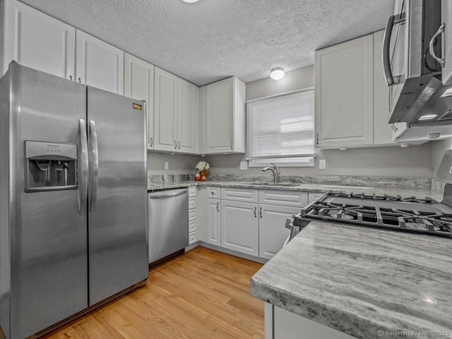 kitchen featuring sink, light stone counters, light wood-type flooring, appliances with stainless steel finishes, and white cabinets