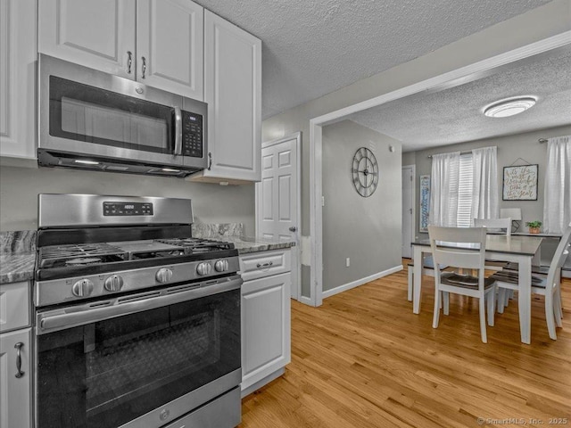 kitchen featuring white cabinetry, appliances with stainless steel finishes, light hardwood / wood-style flooring, and dark stone counters