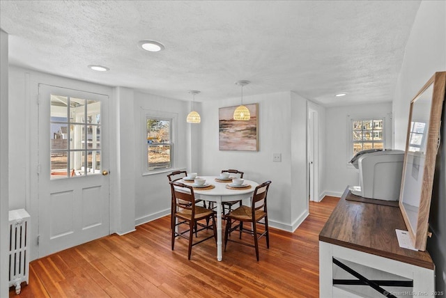 dining room with light wood-style flooring, radiator, baseboards, and a textured ceiling