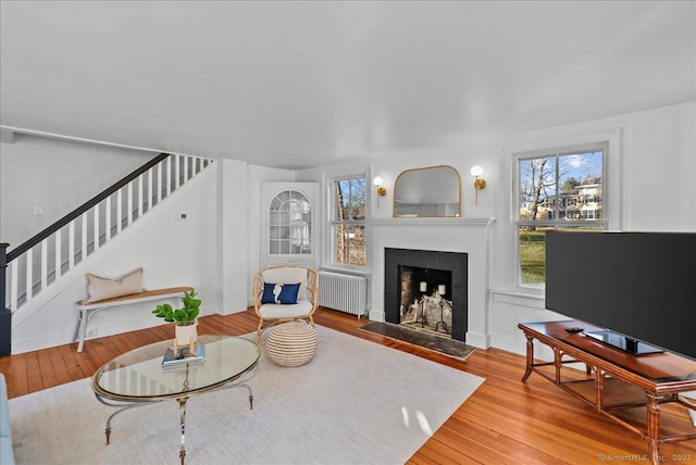 living room featuring baseboards, a fireplace with flush hearth, radiator heating unit, stairs, and wood-type flooring