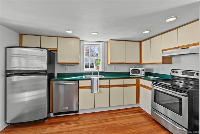 kitchen featuring light wood finished floors, under cabinet range hood, appliances with stainless steel finishes, dark countertops, and cream cabinets