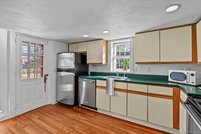 kitchen with a sink, dark countertops, appliances with stainless steel finishes, and light wood finished floors