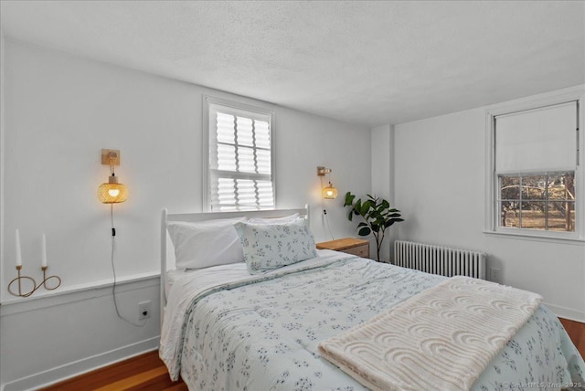 bedroom with a textured ceiling, radiator heating unit, baseboards, and wood finished floors