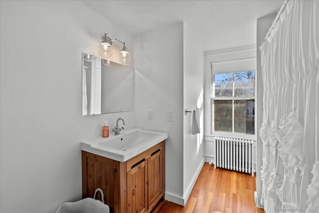 bathroom featuring vanity, radiator, wood finished floors, and baseboards