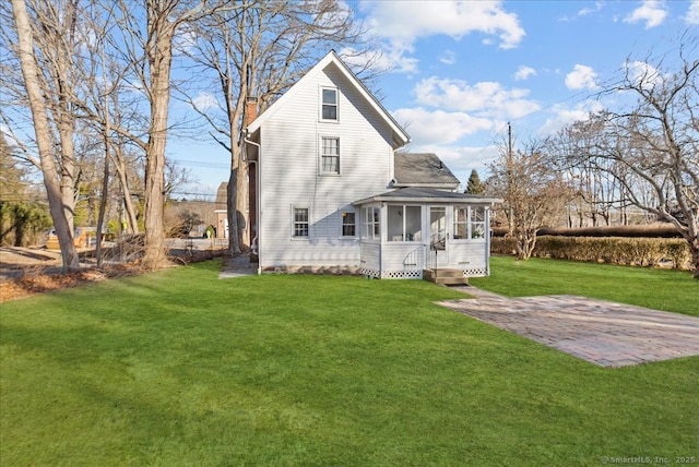 rear view of house featuring a patio, a lawn, a sunroom, and a chimney