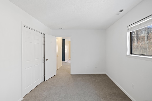 unfurnished bedroom featuring light carpet, a textured ceiling, and a closet