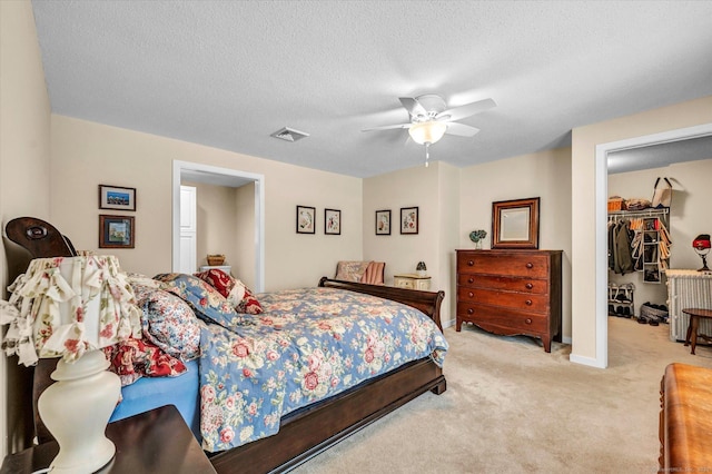 carpeted bedroom featuring ceiling fan, a walk in closet, a closet, and a textured ceiling