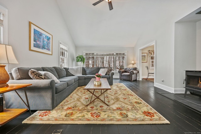 living room featuring dark hardwood / wood-style flooring, ceiling fan, high vaulted ceiling, and a wood stove