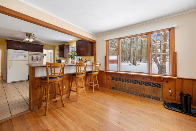 kitchen with white appliances, radiator heating unit, a kitchen breakfast bar, light hardwood / wood-style floors, and kitchen peninsula