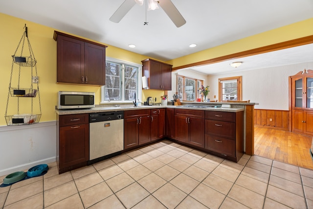 kitchen with light tile patterned flooring, wood walls, kitchen peninsula, ceiling fan, and stainless steel appliances