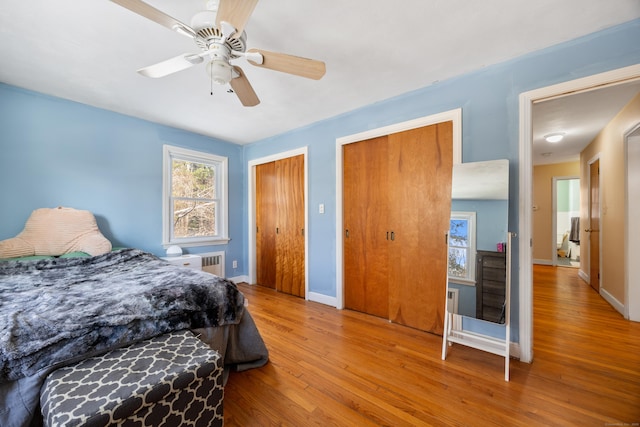 bedroom with multiple closets, ceiling fan, radiator heating unit, and light hardwood / wood-style flooring