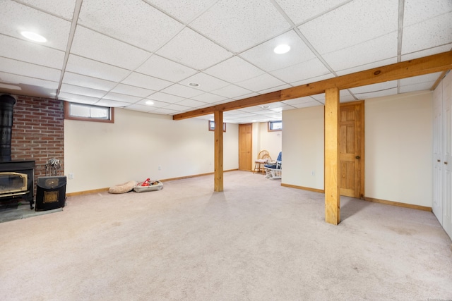 basement with a paneled ceiling, carpet flooring, and a wood stove