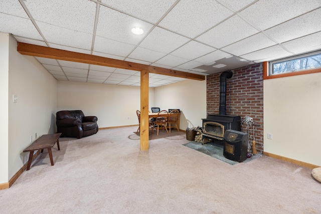 basement featuring a drop ceiling, carpet, and a wood stove