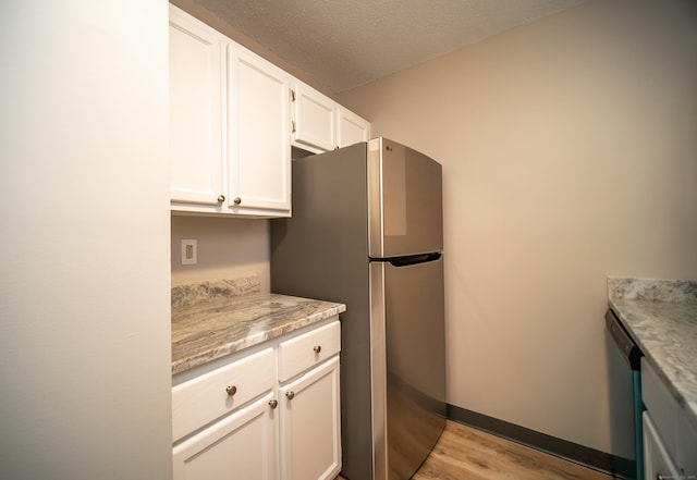 kitchen with appliances with stainless steel finishes, white cabinetry, light stone counters, light hardwood / wood-style floors, and a textured ceiling