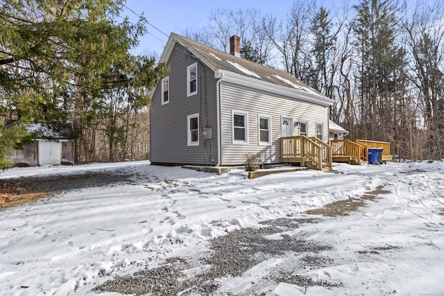 snow covered rear of property featuring a shed