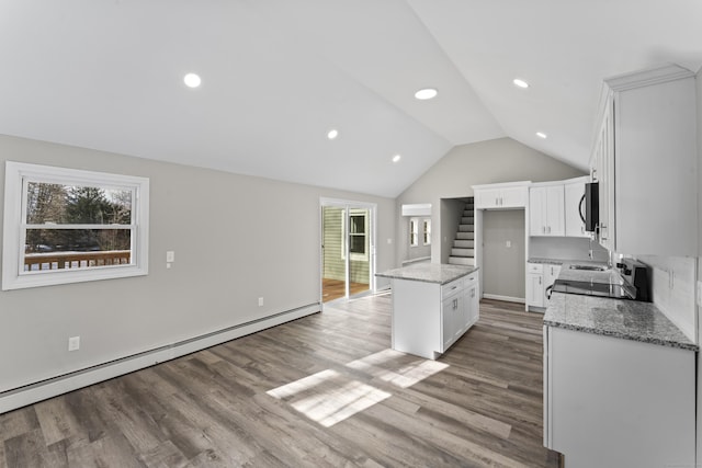 kitchen with a wealth of natural light, white cabinets, a center island, baseboard heating, and light stone countertops