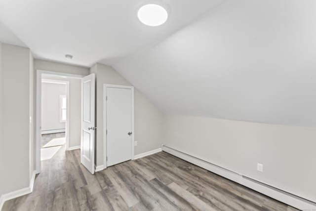 additional living space featuring a baseboard radiator, wood-type flooring, and vaulted ceiling