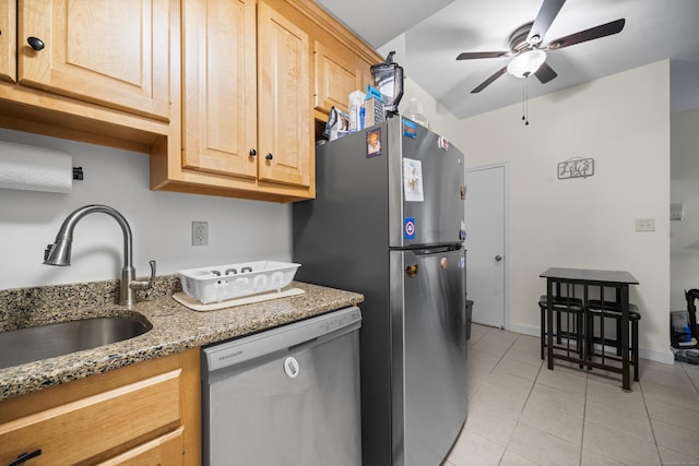 kitchen with light brown cabinetry, sink, dishwashing machine, dark stone counters, and light tile patterned floors