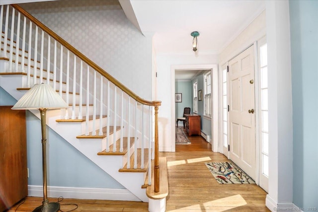 foyer with crown molding, baseboard heating, and light wood-type flooring