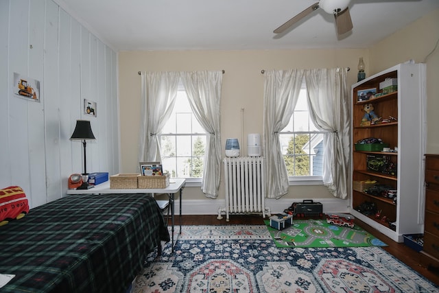 bedroom featuring multiple windows, radiator, wood-type flooring, and ceiling fan