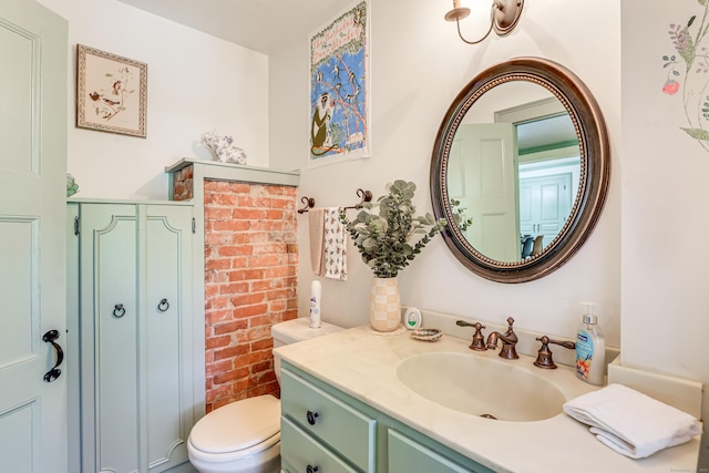 bathroom featuring brick wall, vanity, and toilet