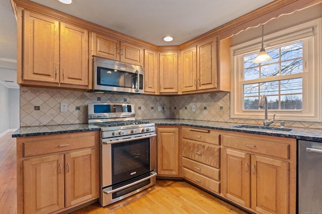 kitchen with sink, appliances with stainless steel finishes, dark stone countertops, decorative light fixtures, and light wood-type flooring