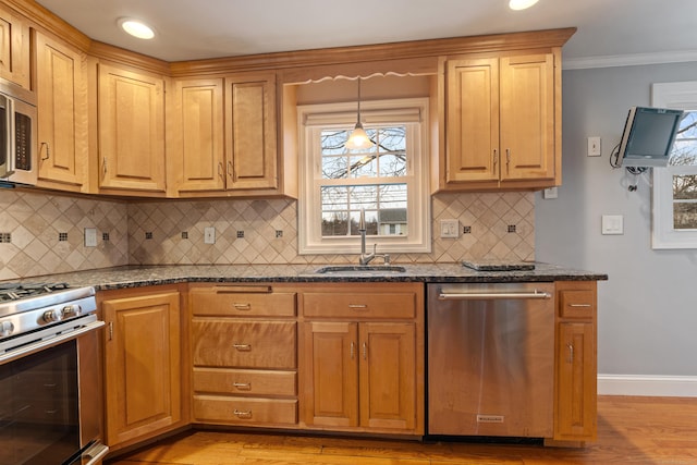 kitchen featuring sink, light hardwood / wood-style flooring, hanging light fixtures, appliances with stainless steel finishes, and dark stone counters