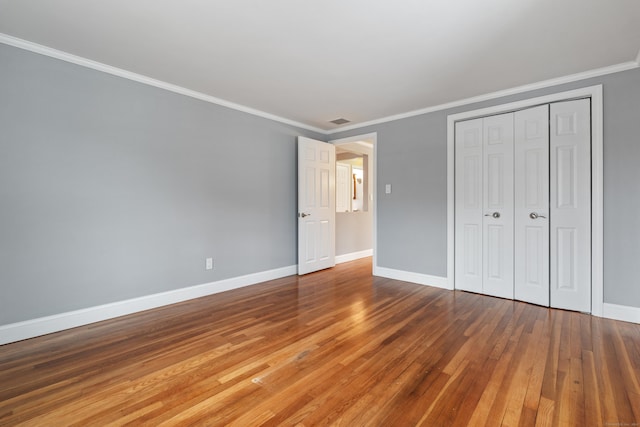 unfurnished bedroom featuring hardwood / wood-style floors, ornamental molding, and a closet