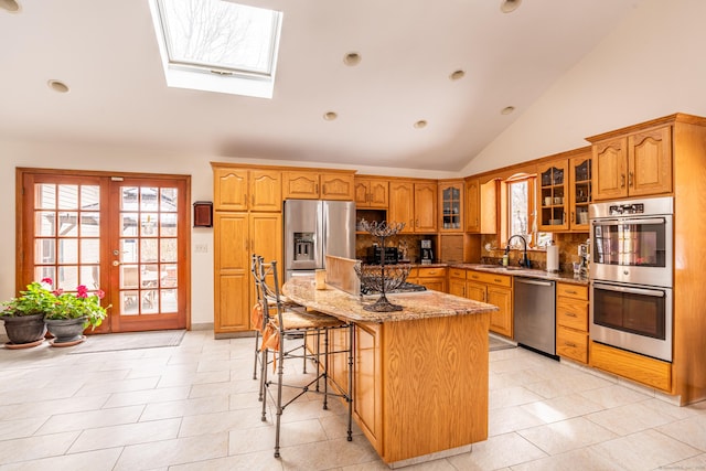 kitchen with sink, light stone counters, appliances with stainless steel finishes, a kitchen breakfast bar, and a kitchen island