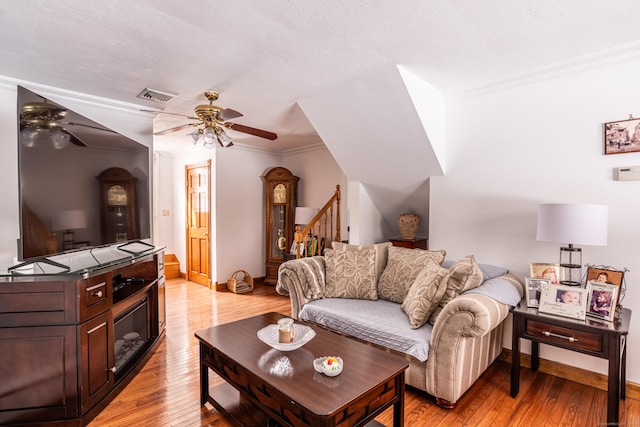 living room with crown molding, light hardwood / wood-style flooring, a textured ceiling, and ceiling fan