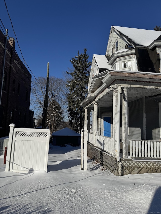 view of snowy exterior with a porch and fence