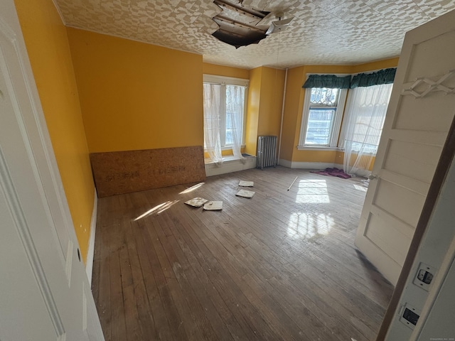 interior space with radiator, a textured ceiling, baseboards, and wood finished floors