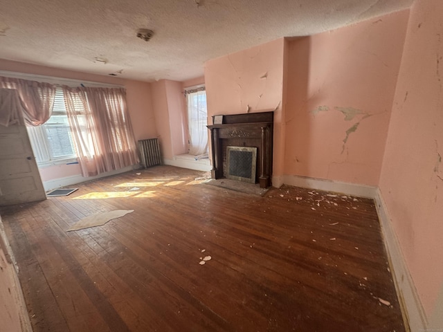 unfurnished living room with a textured ceiling, dark wood-style flooring, a fireplace with flush hearth, and a wealth of natural light