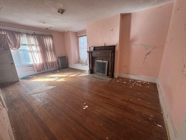 unfurnished living room featuring a fireplace with flush hearth, a textured ceiling, baseboards, and wood finished floors