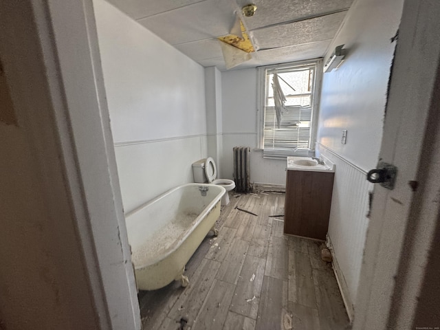 bathroom with radiator, a soaking tub, toilet, a wainscoted wall, and wood finished floors