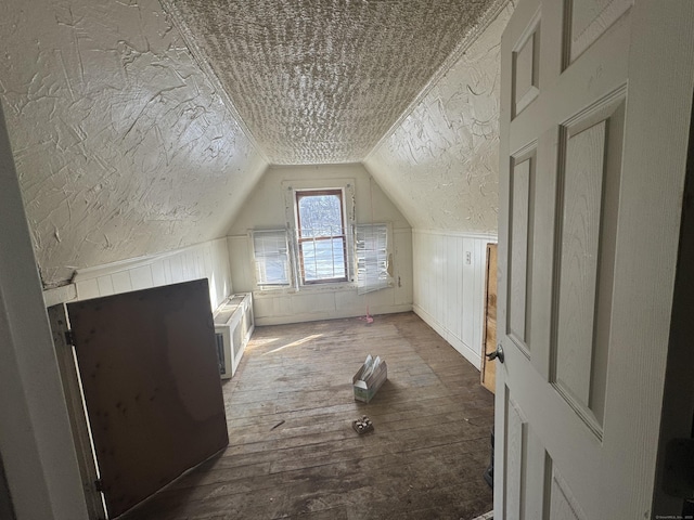 bonus room with lofted ceiling, a wainscoted wall, a textured ceiling, and wood finished floors