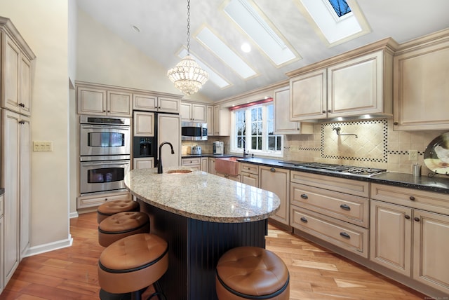 kitchen with pendant lighting, appliances with stainless steel finishes, dark stone countertops, a kitchen breakfast bar, and an island with sink