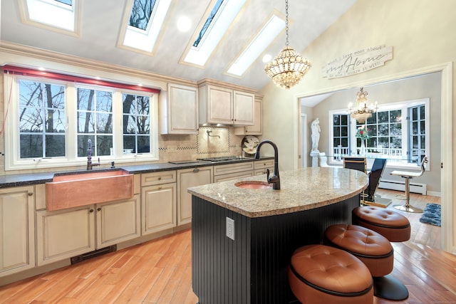 kitchen with vaulted ceiling, decorative light fixtures, sink, a kitchen island with sink, and baseboard heating