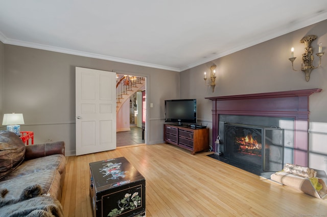 living area featuring stairs, light wood-type flooring, a fireplace with flush hearth, and crown molding