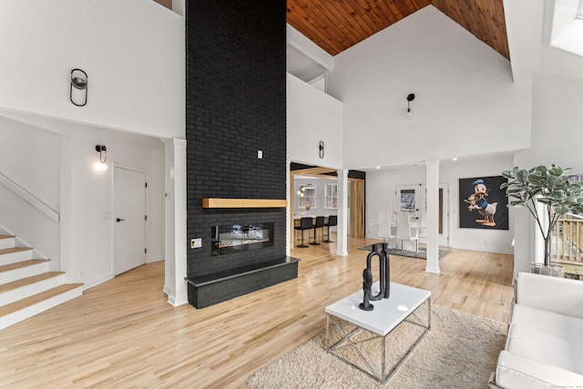 living room with a fireplace, high vaulted ceiling, light hardwood / wood-style flooring, and ornate columns