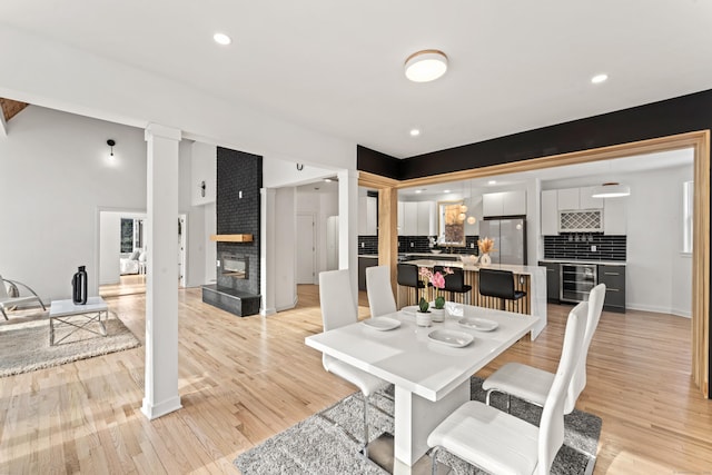 765 Durham Rd, Guilford, CT 06437 - dining space featuring light wood finished floors, decorative columns, a fireplace, and beverage cooler