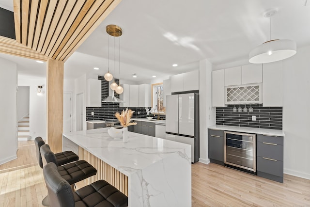 kitchen with white appliances, white cabinetry, hanging light fixtures, wine cooler, and wall chimney exhaust hood