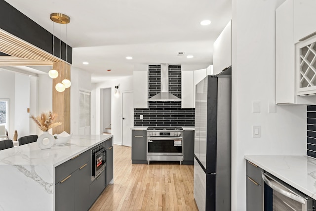 kitchen with wall chimney range hood, gray cabinetry, hanging light fixtures, stainless steel appliances, and white cabinets