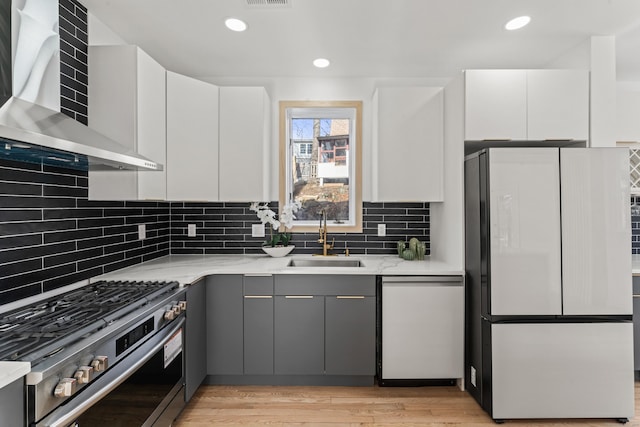 kitchen with wall chimney range hood, gray cabinets, stainless steel gas range, refrigerator, and white cabinetry