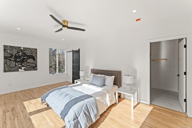 bedroom with light hardwood / wood-style flooring, a barn door, and ceiling fan