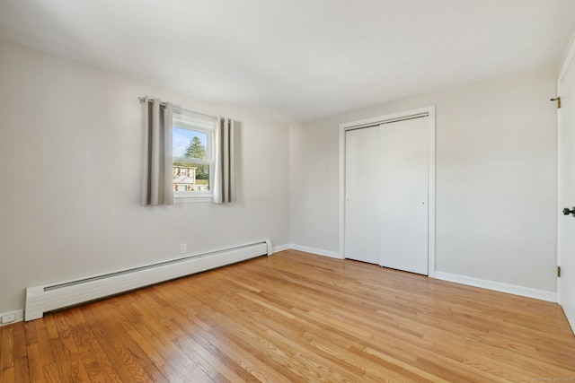 unfurnished bedroom featuring a baseboard radiator, light hardwood / wood-style floors, and a closet